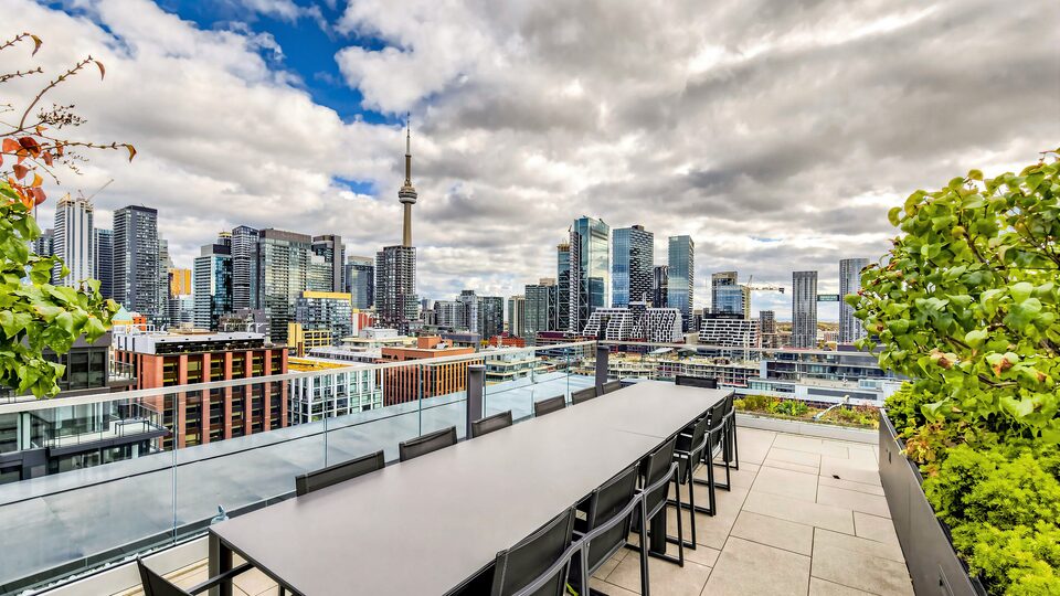 Long communal table on the rooftop terrace with the CN Tower and downtown Toronto skyline behind it