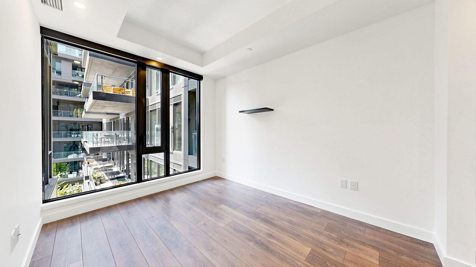 The same primary bedroom unfurnished, with a large window overlooking the courtyard